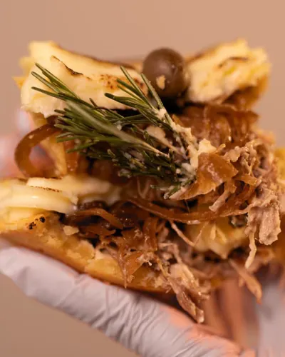 Torta aberta com carne desfiada, cebola caramelizada, creme e um ramo de alecrim
